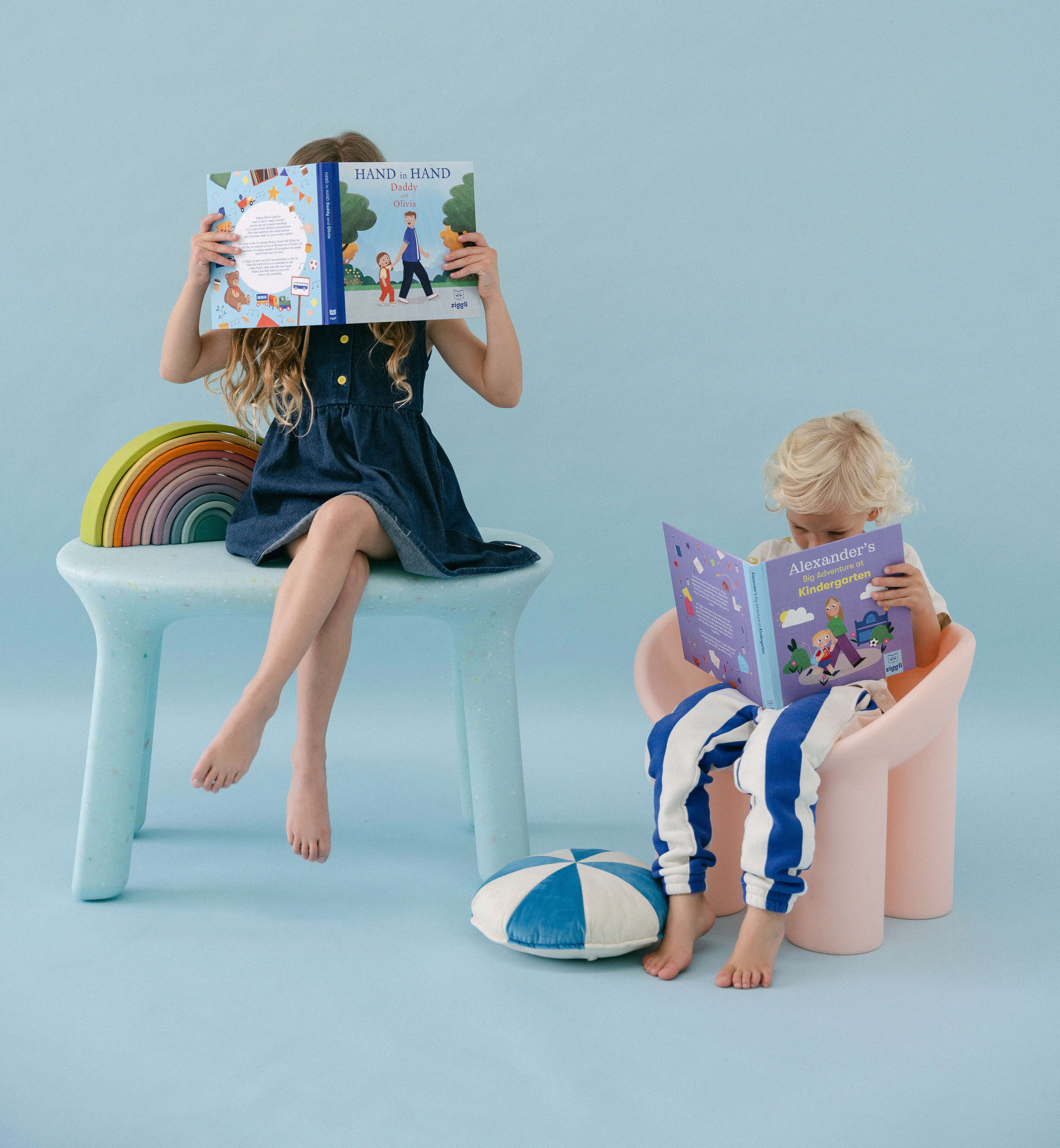 Two children sitting on colourful stools reading personalised children's books against a light blue background