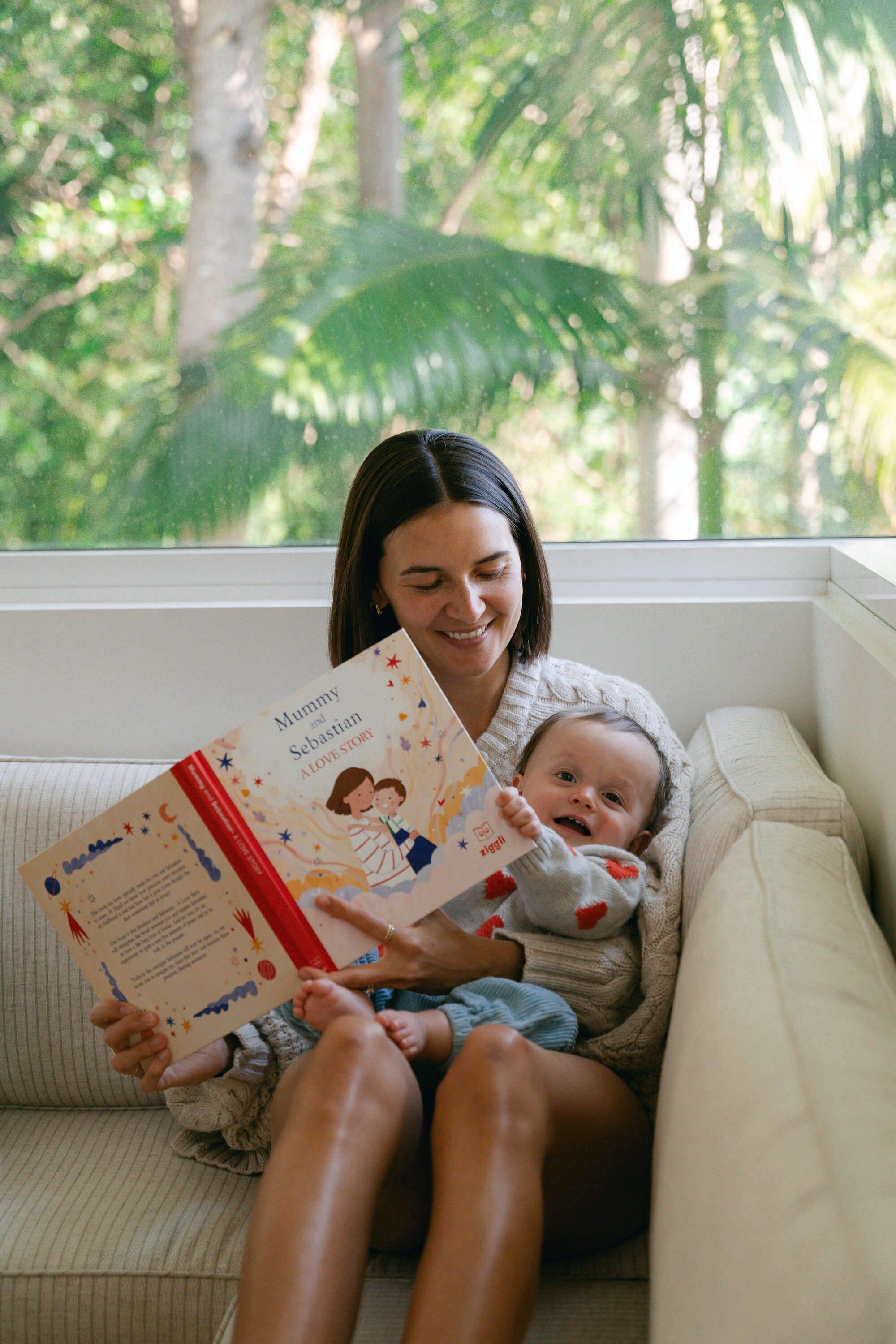 Woman reading a personalised book to a baby on a couch with a natural background