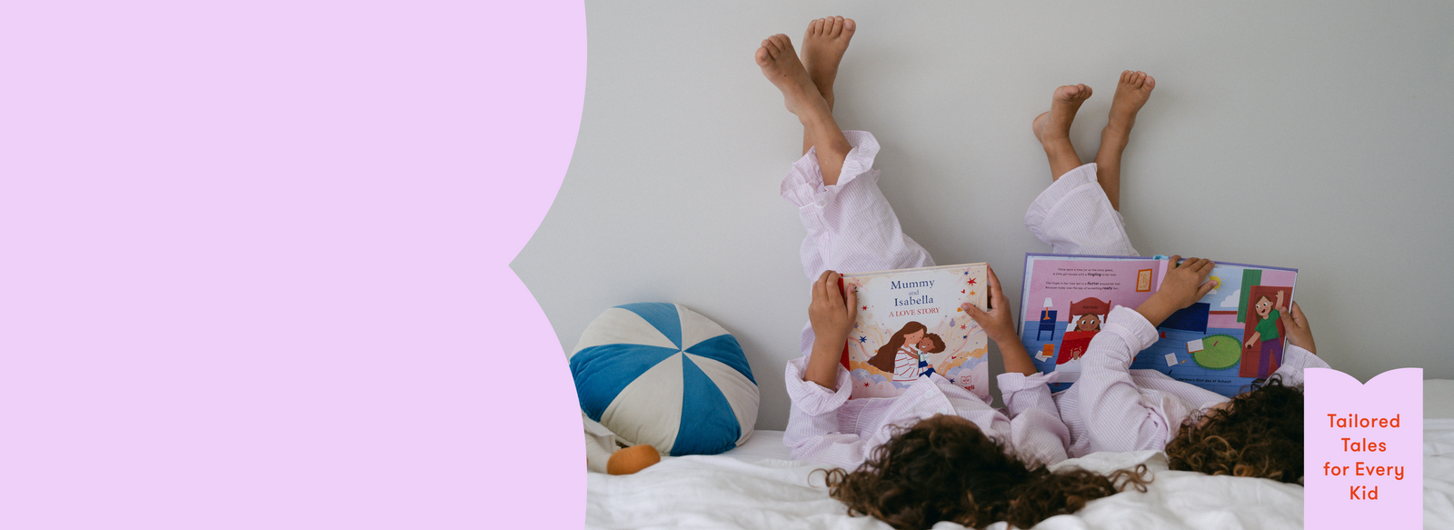 Two children lying on a bed reading personalised books with a colourful pillow and light purple wall in the background.